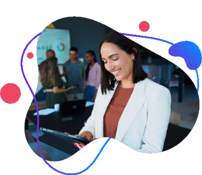 Uśmiechnięta kobieta biznesu korzystająca z&nbsp;tabletu w&nbsp;biurze z&nbsp;zespołem w&nbsp;tle.